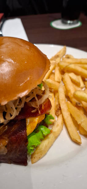 istock Delectable burger with cheese, bacon, and crispy fried onions, served alongside golden fries, on a grill restaurant's table, emphasizing the meal's presentation and appetizing appeal 2196154353