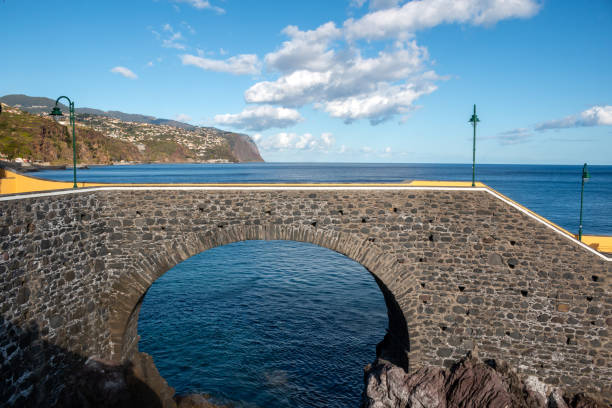 Stone bridge as a pier to the Atlantic ocean. Blue sky with white clouds. Ponta do Sol, Madeira, Portugal.