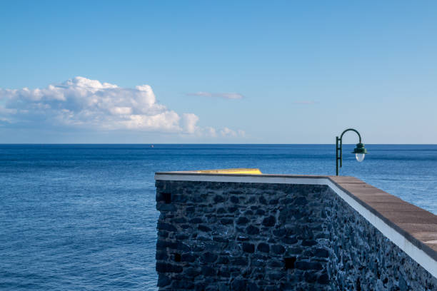 Stone bridge as a pier to the Atlantic ocean. Blue sky with white clouds. Ponta do Sol, Madeira, Portugal.