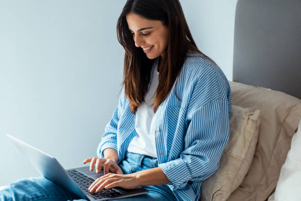 istock One adult womqan using laptop sitting on bed, relaxing for work or leisure activity. Chatting with friends, online connection. People and technology. Remote worker on travel hotel room 2196155703