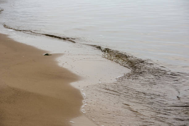 a sandy beach with a line of small waves washing the shore.