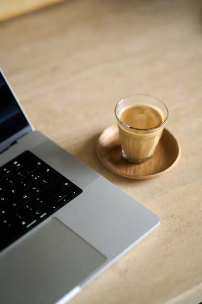 Cortado coffee sits next to a laptop computer on a desk, suggesting a productive work-from-home setup