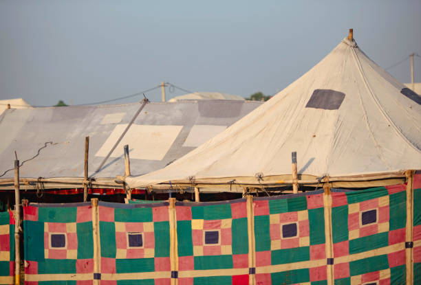 A yellow quilted historical vest hanging on a rope in front of a canvas tent at a historical reenactment camp. Traditional medieval or early modern clothing detail, capturing the authentic atmosphere of a living history event