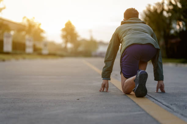 istock person in runner starting position on road. back view, blurred background featuring trees and early morning sun. 2196177217