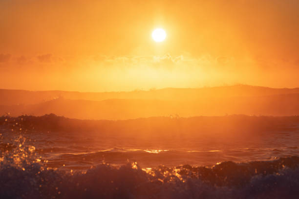 Breathtaking sunset with a large glowing sun setting over the ocean, casting vibrant orange hues across the sky and waves. Ideal for nature, seascape, and tropical travel concepts.