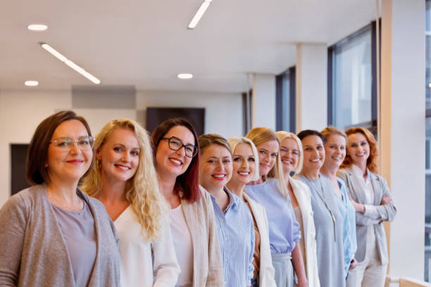 Portrait of female colleagues standing side by side at office and smiling at camera.