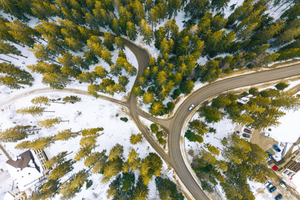 Aerial view of car driving on a curved highway in a snowy mountain, with the intersection of two side roads.