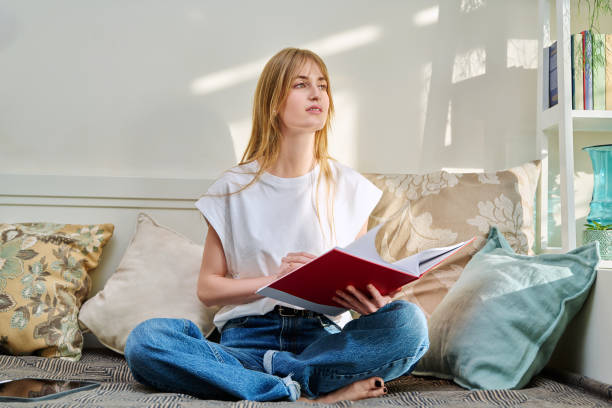 istock Portrait of female student sitting on couch with notebook, studying at home 2196200611