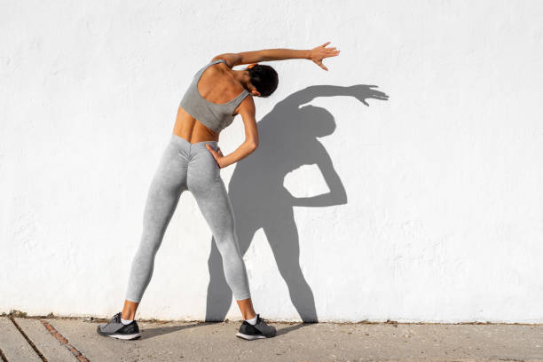istock Athletic woman standing in a confident pose against a white wall, showcasing her back muscles, with strong sunlight casting bold shadows. 2196202626