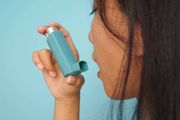 istock Young Woman Administering Asthma Medication with Inhaler on blue background 2196203246