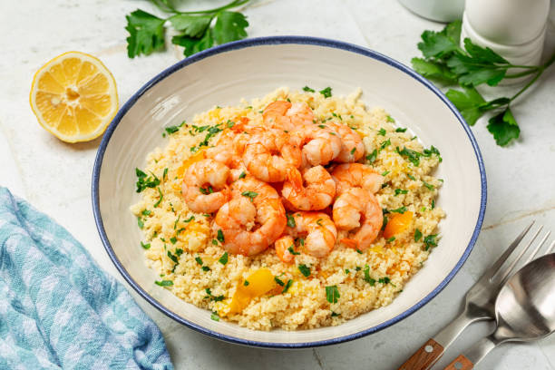 istock A plate with Couscous and fried Shrimps, yellow tomatoes, onion, parsley. White table surface, blue napkin. 2196205424