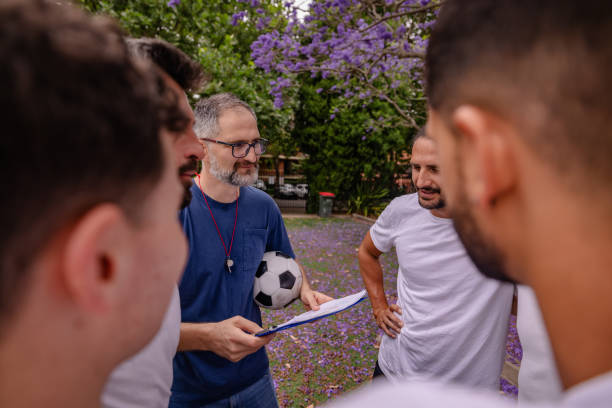 A diverse group of men gathers in a lush park in Sydney to discuss soccer strategies. Excitement fills the air as they prepare for an engaging practice session together.