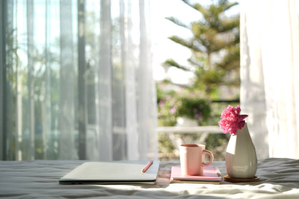 Coffee cup and notebooks on bed with cozy windows view