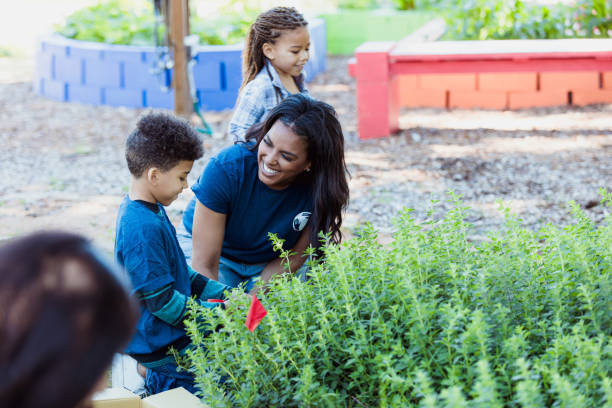 istock Volunteer teacher assisting elementary school students in a community garden 2196224730
