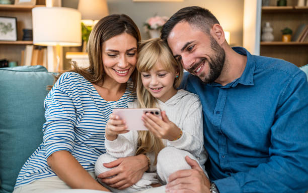 istock Happy parents and daughter having fun with smartphone at home 2196225663