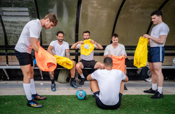 Group of young men in Sydney gathers on a soccer field, getting ready for practice by changing into jerseys and sharing smiles, showcasing team spirit and enthusiasm.