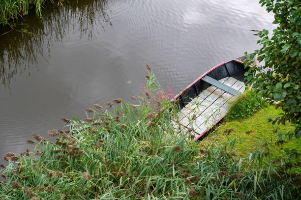 Small boat lies in the water, on the bank of a river