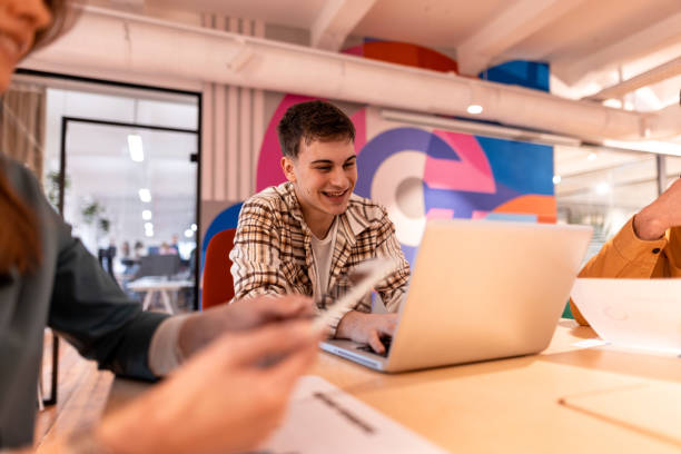 istock Young man working on laptop with colleagues in modern office 2196235401