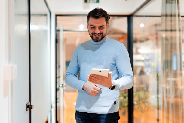 istock Smiling businessman walking in office corridor and using digital tablet 2196235578