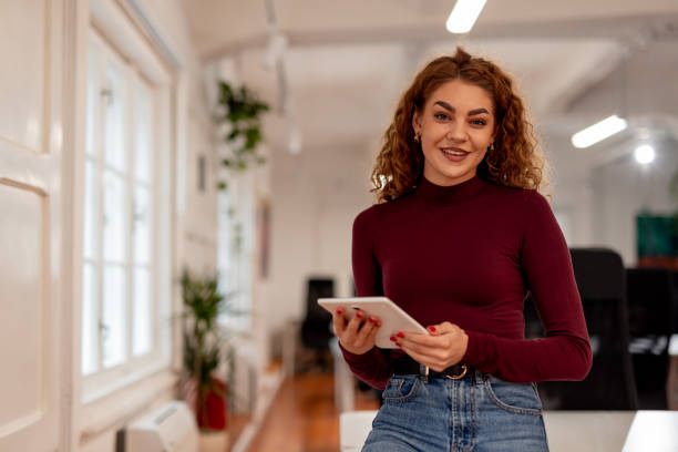 istock Smiling Woman Standing in Office Holding a Tablet in a Casual Environment 2196235948