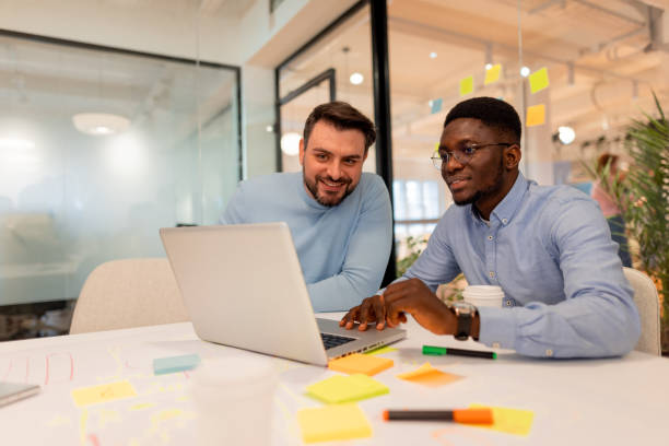 istock Two smiling businessmen working together on a laptop in the office 2196236534