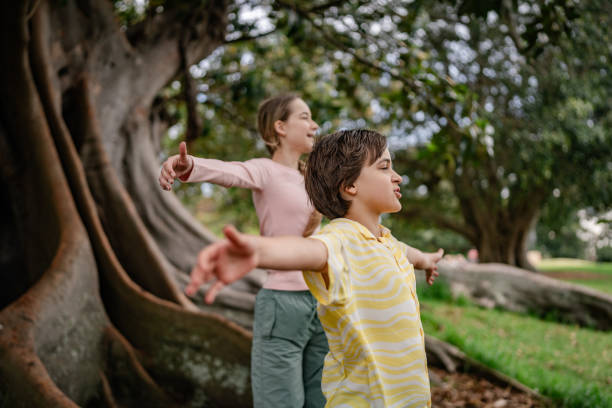 Two children in summer looking examining tree bark through magnifying glass while exploring forest nature and environment on sunny day