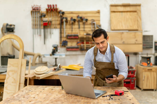 istock Mid adult carpenter man using mobile phone and laptop at carpentry 2196238535