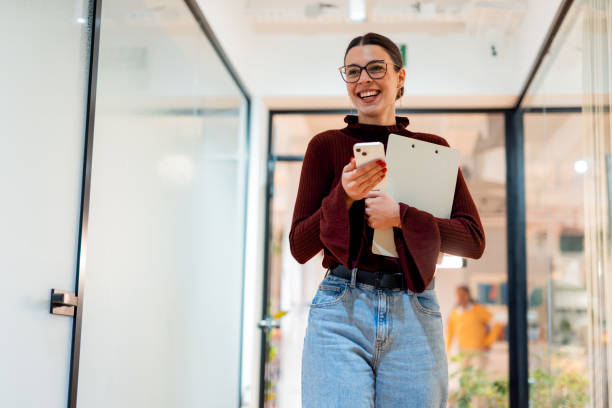 istock Young businesswoman walking in office corridor and using smartphone 2196238980