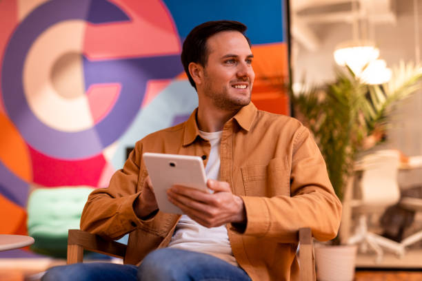 istock Creative businessman holding tablet and looking away, sitting in modern office 2196239461