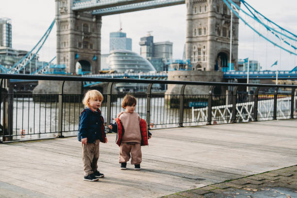 Two toddlers standing on a wooden walkway, enjoying the view of the iconic Tower Bridge in London, United Kingdom