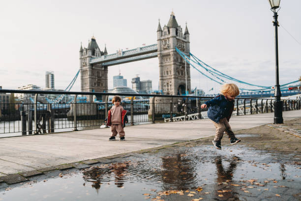 Two children joyfully playing and jumping in puddles beside Tower Bridge, capturing the essence of childhood fun in London, UK