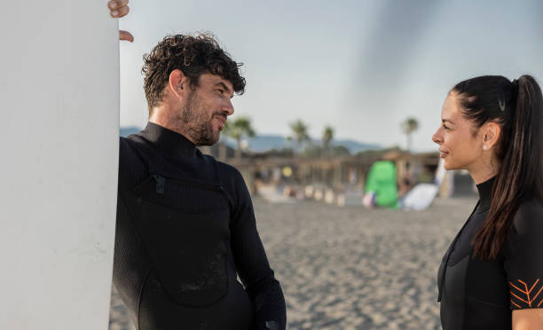 istock Surfers wearing wetsuits talking on the beach on a sunny day 2196241223