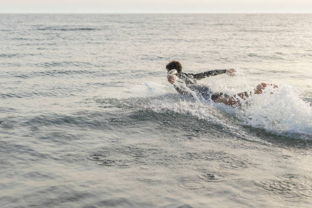 A moment captured where a surfboard, adorned with colorful patterns, emerges from the crest of frothy ocean waves. The image emphasizes the movement and energy of the aquatic environment.