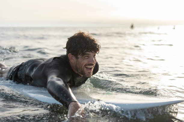istock Surfer paddling and smiling on surfboard in ocean at sunset 2196241301