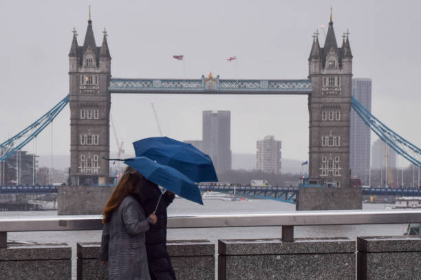 London, UK - January 27 2025: People walk with umbrellas along London Bridge past Tower Bridge on a rainy, windy day.