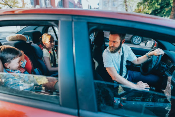 Caring father driving his two children home after school. The young boy and girl sit safely in the back seat, wearing seat belts, while the father looks back to check on them.