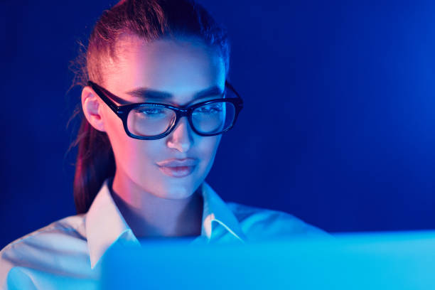 Young Woman Working on Computer Screen in Low Light With Blue and Purple Hues