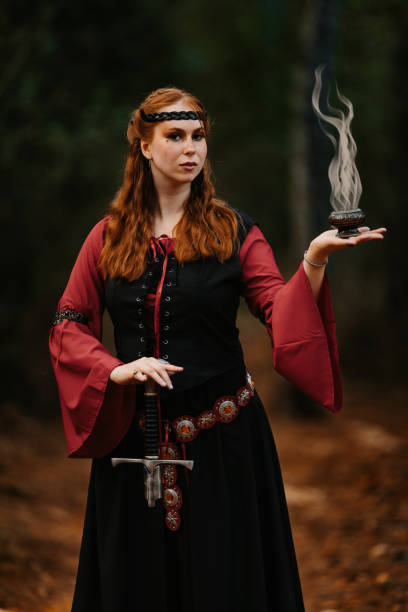 Portrait of a red-haired beautiful medieval fantasy in a misty forest witch performs a ritual while holding a censer and a sword