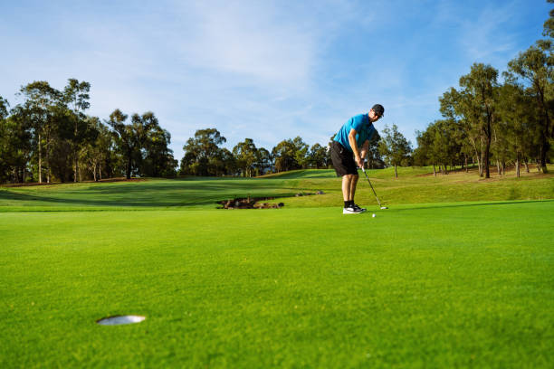 istock Golfer in casual clothing putting on a lush green golf course surrounded by trees under a clear blue sky 2196258201