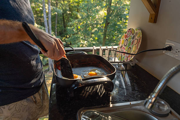 Individual flipping eggs in a frying pan in a sunlit kitchen. Forest view from the window. Home cooking experience in a modern kitchen setting.
