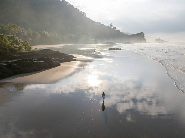 istock Woman Strolling on Serene Beach at Sunrise 2196264116