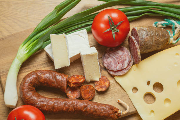 Bright sliced sausages and cheeses with vegetables and herbs lie on a board