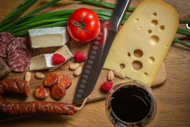 Bright sliced sausages and cheeses with vegetables and herbs lie on a board