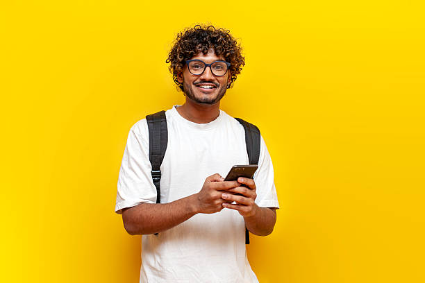 istock young indian guy student in glasses with backpack using smartphone on yellow isolated background 2196270017