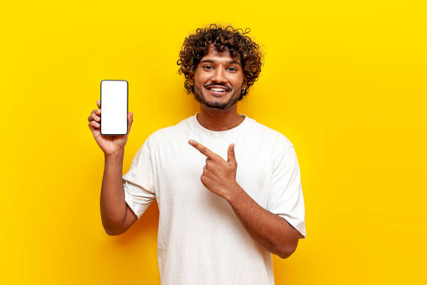 istock young indian guy pointing at blank smartphone screen on yellow isolated background, south asian man in white t-shirt 2196270040