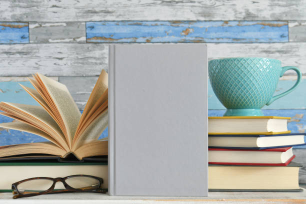 Blank hardcover book cover for mock up in front of a stack of books with teacup and glasses