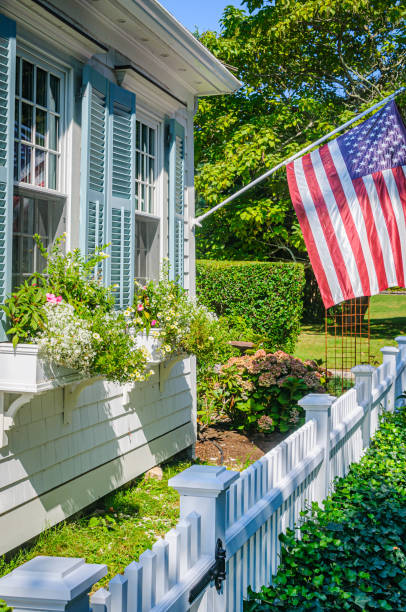 Sandwich, Massachusetts, USA -September 5, 2024 -Blue shuttered windows frame overflowing window boxes beside an American Flag on a old Cape Cod home.