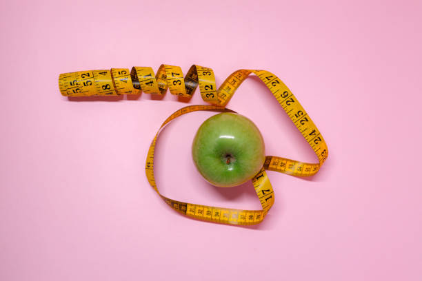 istock Fresh green apple surrounded by measuring tape on pink background 2196276109