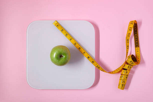 istock Weighing a green apple on a scale surrounded by a measuring tape 2196276110