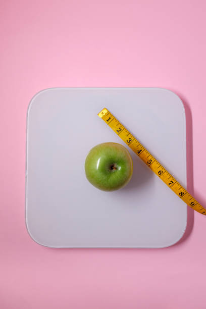 istock Measuring a green apple with a tape measure on a pink surface 2196276276
